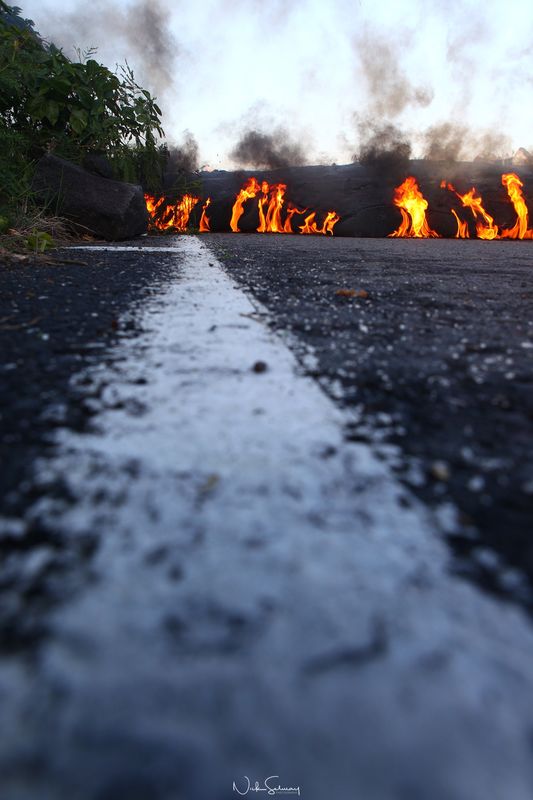 In this image of hot lava, lava burns a road on the edge of Volcano National Park in HI. Shop this print & a variety of hot lava photography for sale.
