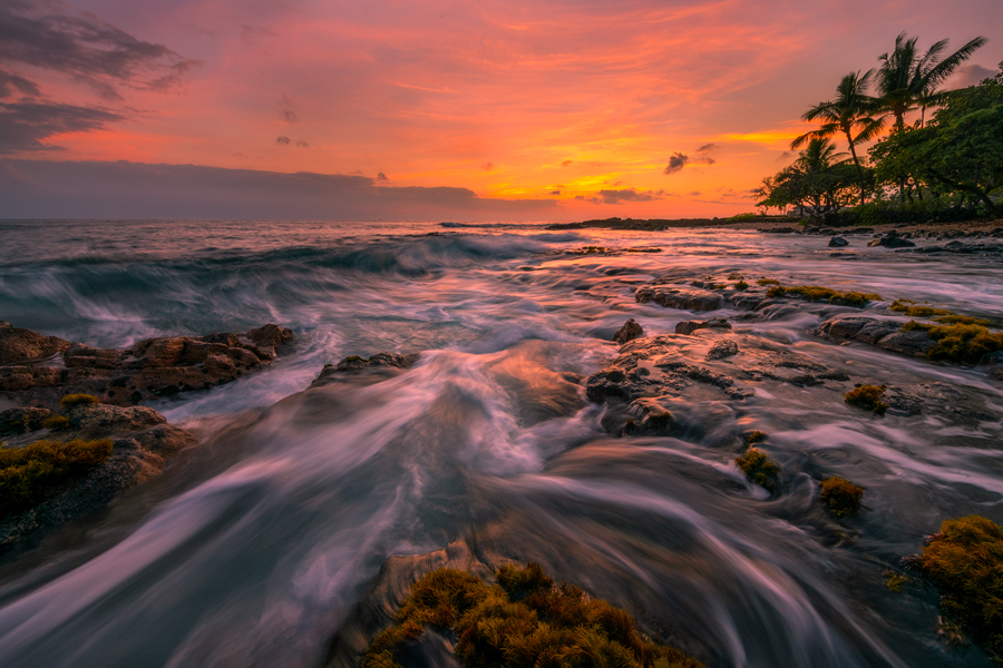 Water rushes back into the ocean as the sun dips below the horizon.