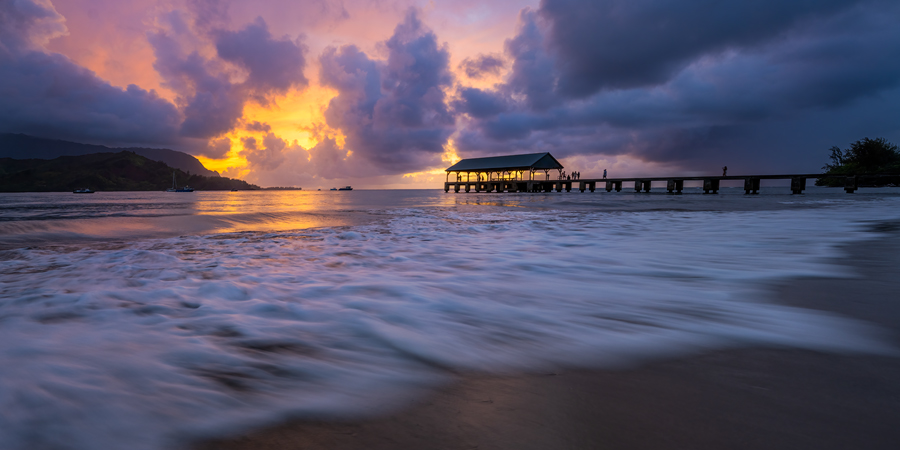 A brilliant sunset erupts with color with the famous Hanalei Pier in the distance.The pier was originally built of wood before...