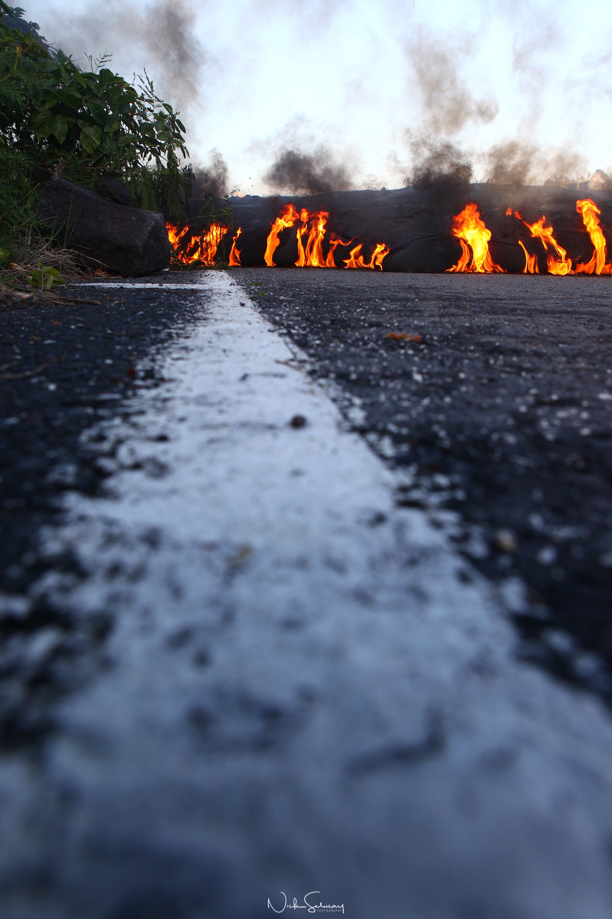 In this image of hot lava, lava burns a road on the edge of Volcano National Park in HI. Shop this print & a variety of hot lava photography for sale.