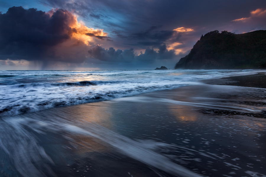 A winter storm at sunrise creates a dramatic scene reflecting across the unique black sand beach of Pololu Valley.