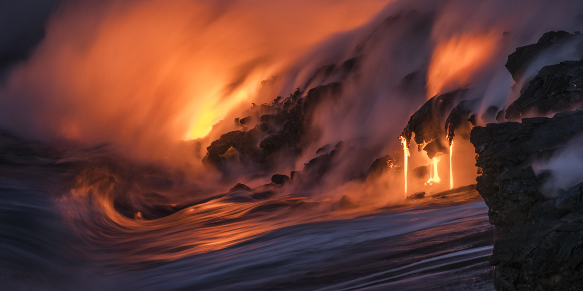 Lava pours into the Pacific Ocean as the waves crash against it.